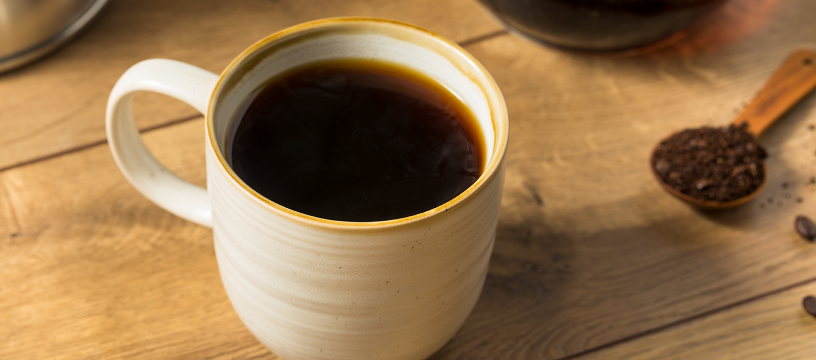 Warm ceramic mug filled with freshly brewed His Word Coffee on a wooden table, next to a scoop of ground beans—highlighting small-batch freshness and handcrafted quality.