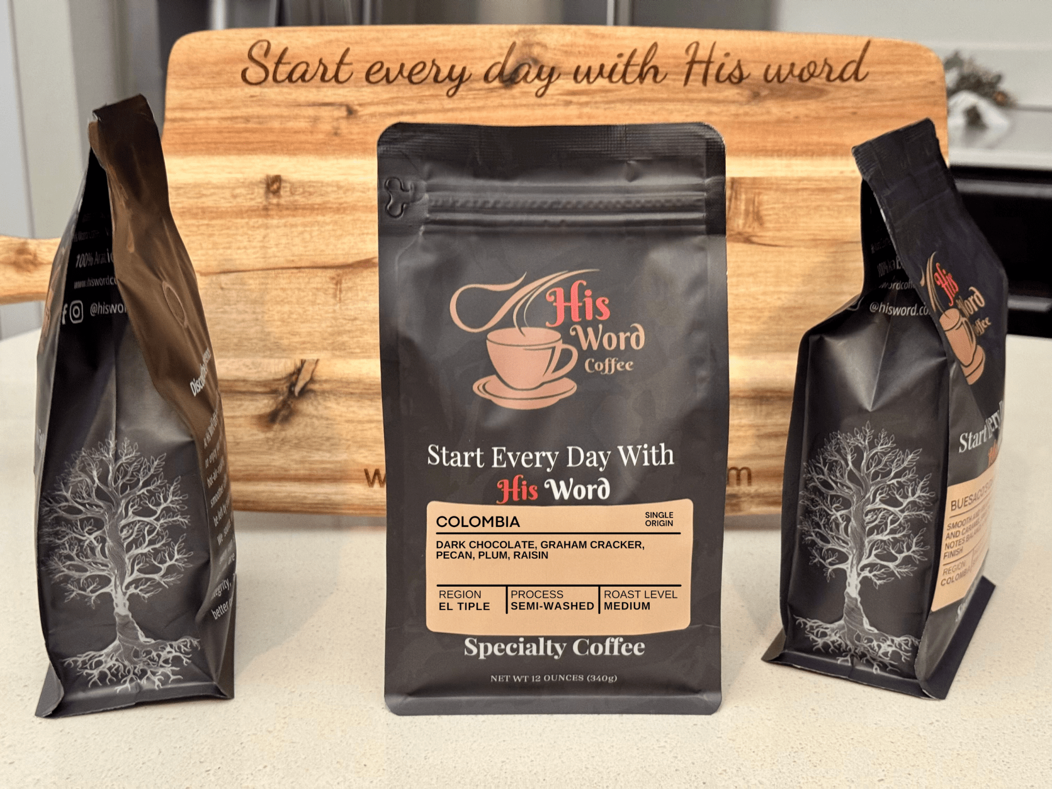 Three Colombia coffee bags in front of a Scripture board, highlighting dark chocolate, graham cracker