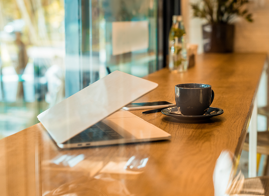 A cup of His Word Coffee beside a partially closed laptop on a wooden counter, bathed in natural light—ideal for devotional journaling, focused work, or creative moments.