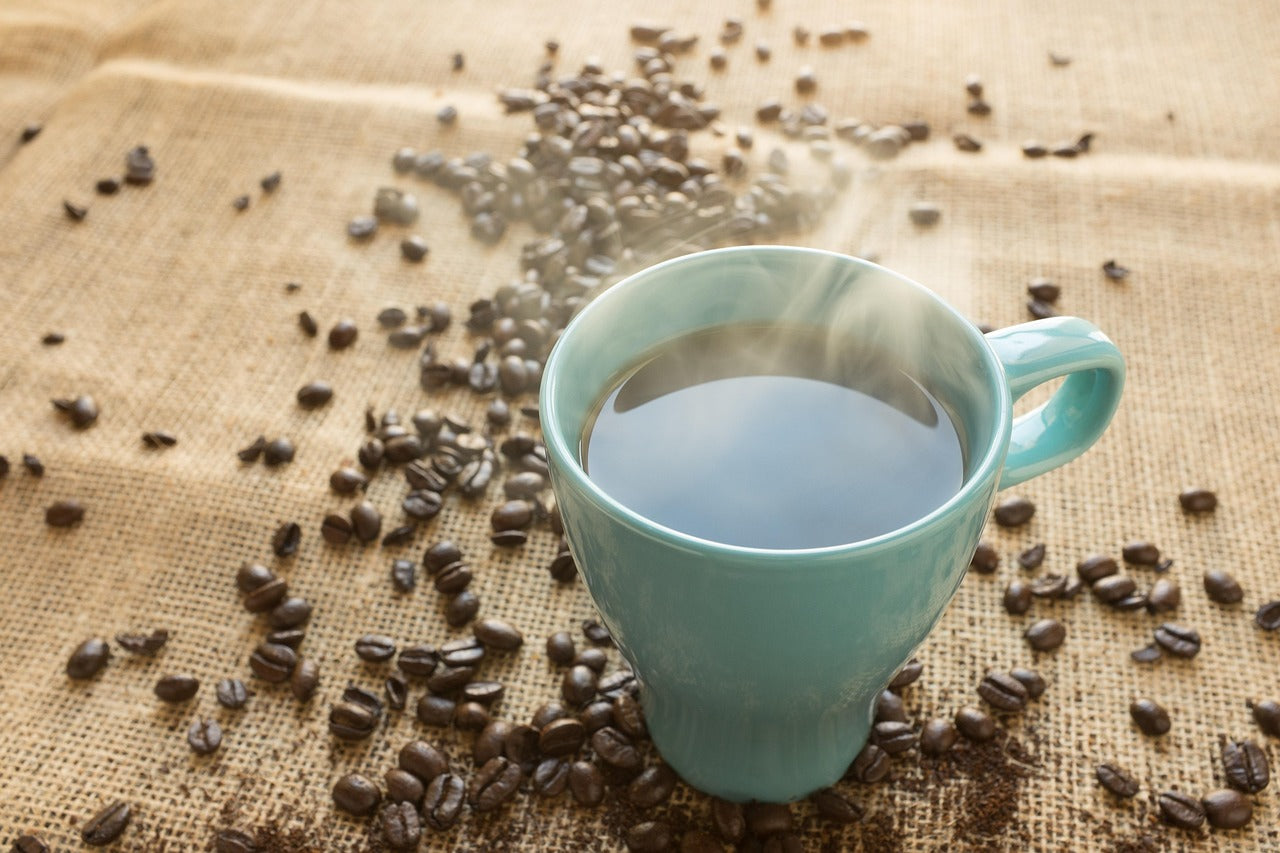 A cup of dark roast low acid coffee surrounded by fresh roasted coffee beans