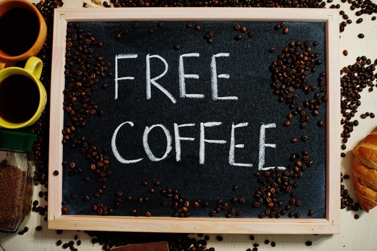 Chalkboard sign reading Free Coffee surrounded by coffee beans and colorful mugs on a table - His Word Coffee
